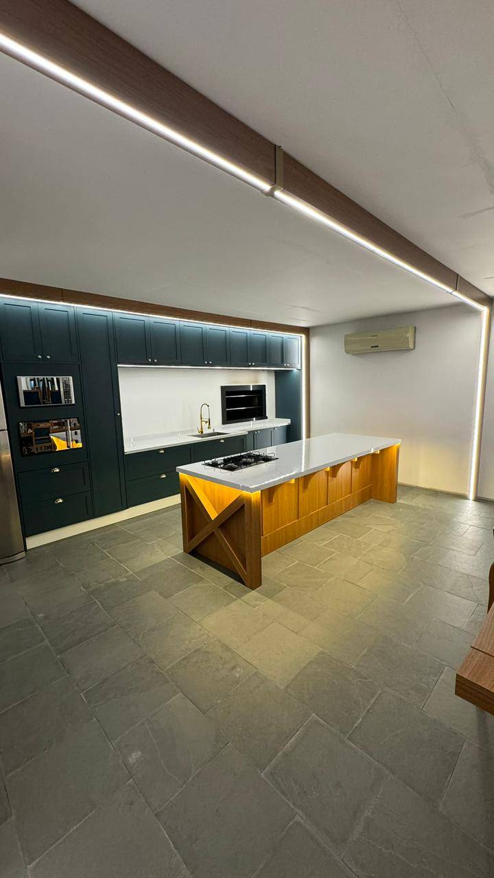 Área gourmet com bancada em L e iluminação suspensa.